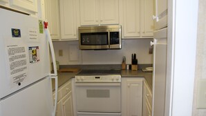 A compact kitchen with white cabinets, a stainless steel microwave, a white refrigerator, and a stove.