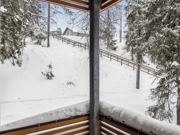 Un espace extérieur enneigé avec une terrasse en bois, des arbres couverts de neige et une rambarde en métal.