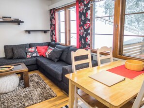 Un salon chaleureux avec un canapé d’angle, une table à manger en bois et une vue sur un paysage enneigé, visible à travers de grandes fenêtres.