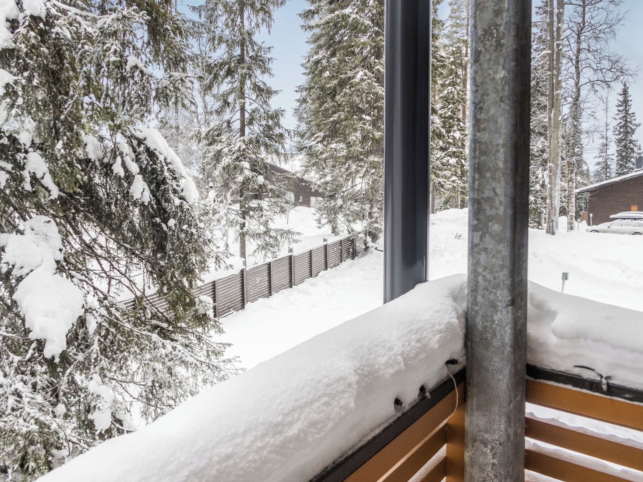 A snowy landscape with a wooden bench and a metal railing, overlooking a snow-covered area with trees and a building.