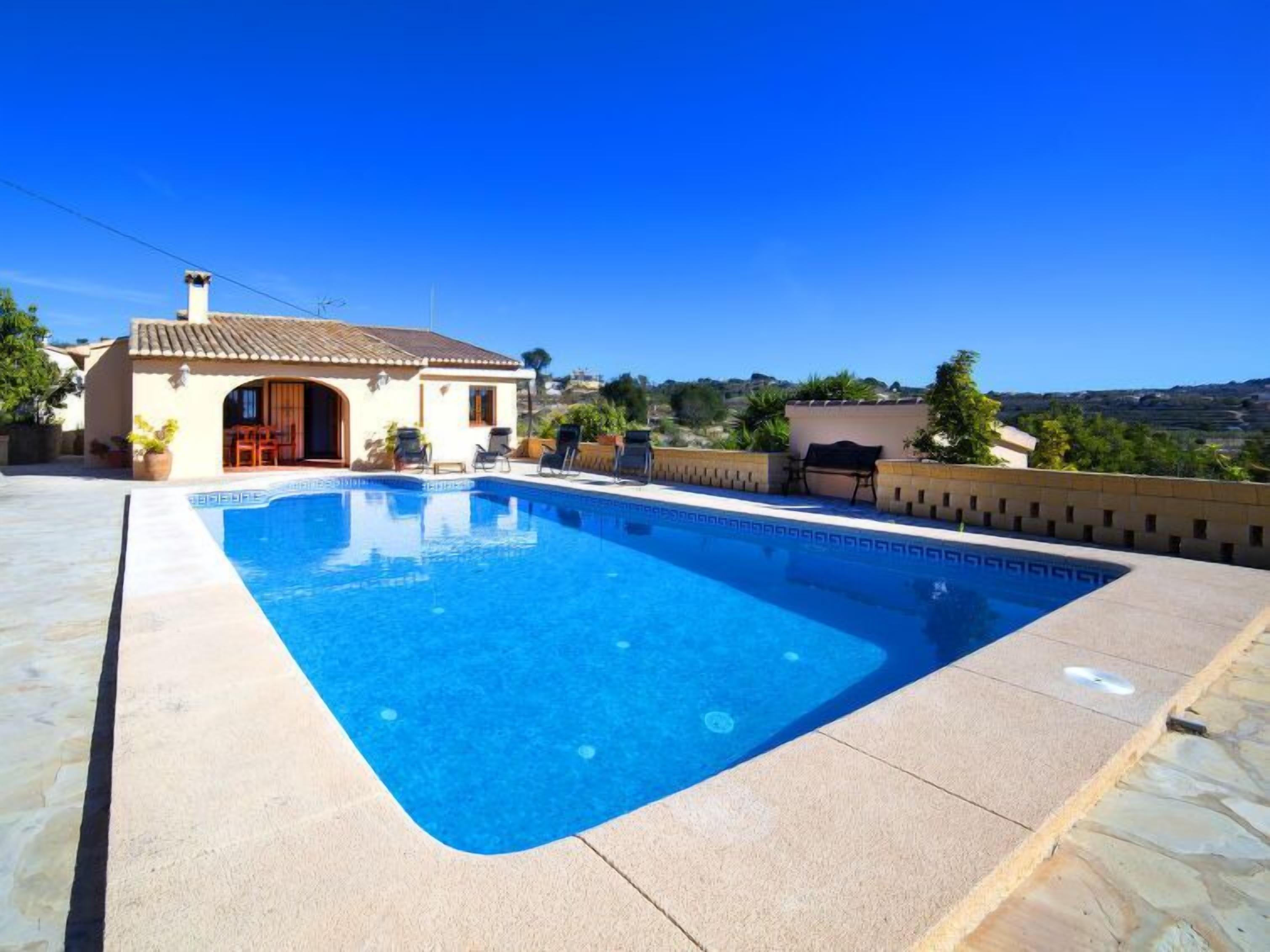 Ein rechteckiger Pool mit einer gefliesten Liegefläche, ein kleines Gebäude mit einem Ziegeldach und ein Blick auf die Landschaft im Hintergrund.