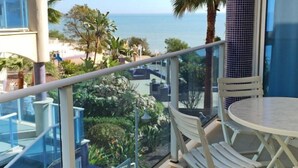 A balcony with a view of the ocean, white outdoor furniture, and a glass railing.