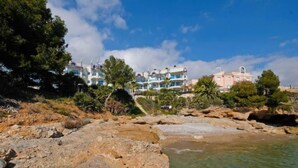 A coastal hotel with multiple balconies overlooking the sea, surrounded by rocky terrain and greenery.