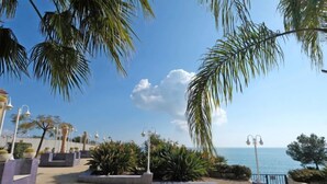 A paved outdoor area with palm trees, street lamps, and a view of the sea.