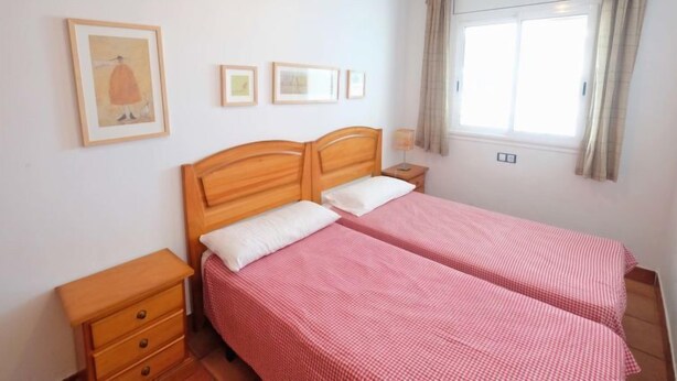 A room with two single beds, a wooden nightstand, a small drawer, and a window with curtains.