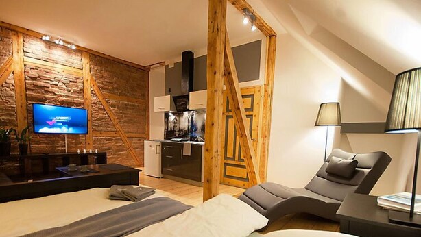 A modern hotel room with a large bed, a sofa, a TV, and a kitchenette.