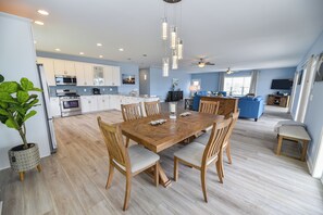 Une cuisine spacieuse équipée d’appareils modernes, un coin repas avec une table et des chaises en bois, et un salon avec un canapé et une télévision.