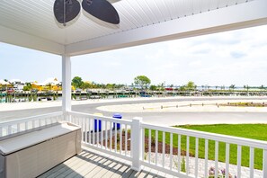 A covered outdoor area with a white railing, a bench, and a view of a marina with boats and a road. - Stunning-waterfront, beach, pools, family fun & pets! (Long Neck)