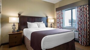 A hotel room with a large bed, two bedside tables with lamps, a window with patterned curtains, and a view of the outside. - Amazing Resort at Mt. Olympus Water & Theme Park with FREE Passes! (Wisconsin Dells)