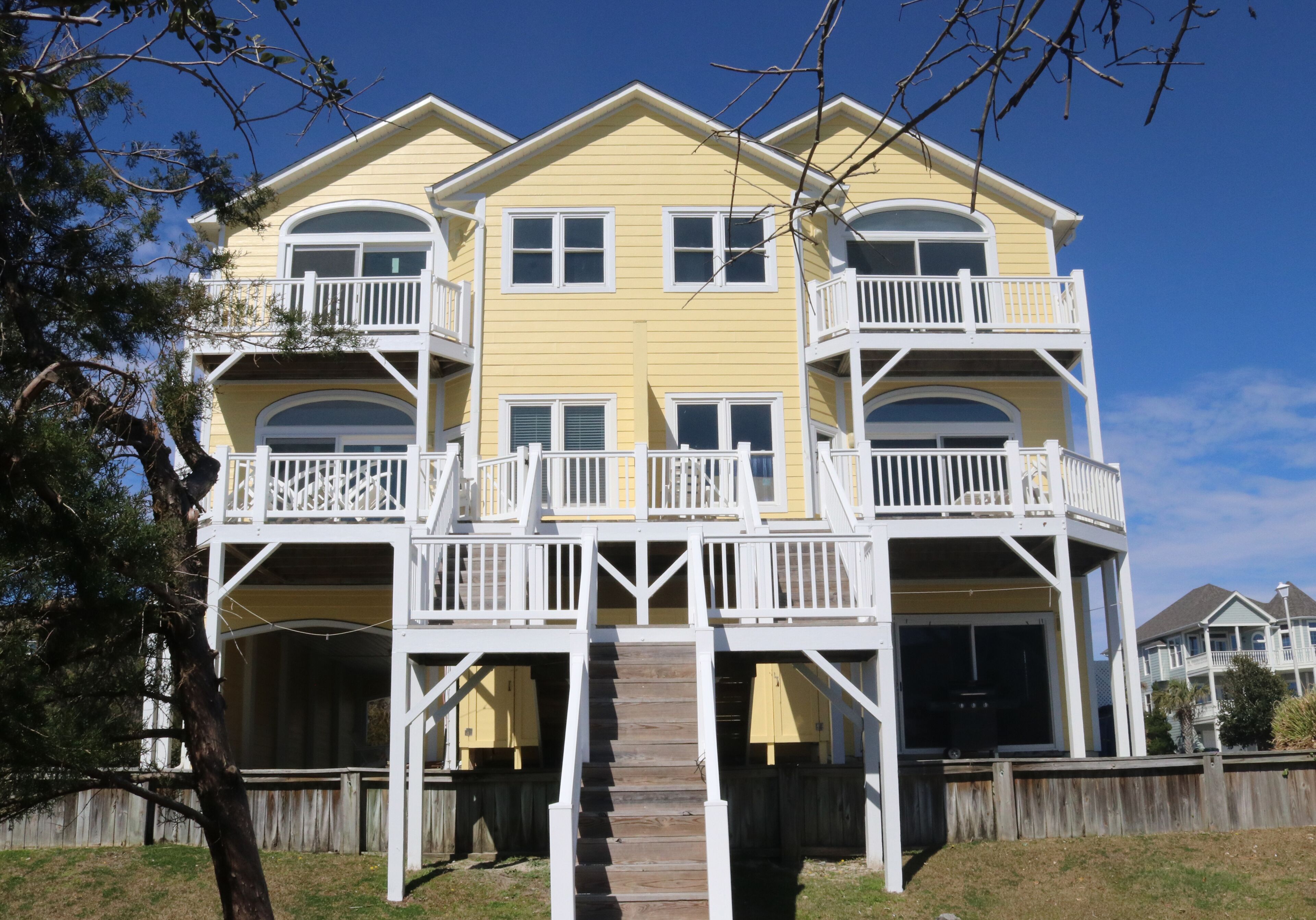 A multi-story yellow building with balconies, a wooden deck, and a staircase leading to the entrance.