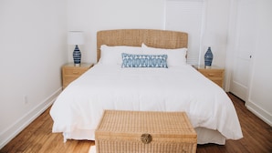A neatly arranged bedroom with a large bed, two bedside tables, and a wicker chest of drawers. - Historic 3 bedroom Cottage for 8 with pool -walk to the beach! (Tybee Island)