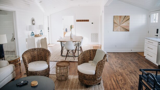 A spacious living area with wicker furniture, a dining table, and a kitchen area. - Historic 3 bedroom Cottage for 8 with pool -walk to the beach! (Tybee Island)