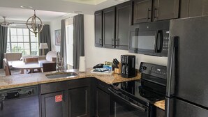 A modern kitchen with black appliances, a granite countertop, and a dining area with a table and chairs. - Spacious Branson  lodging with Beautiful scenery (Branson)