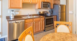 Compact kitchen area with a dishwasher, microwave, oven, and refrigerator. Features a sink, coffee maker, and seating for two.
