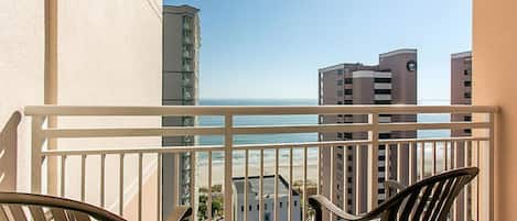 A balcony with a view of the ocean and adjacent buildings.