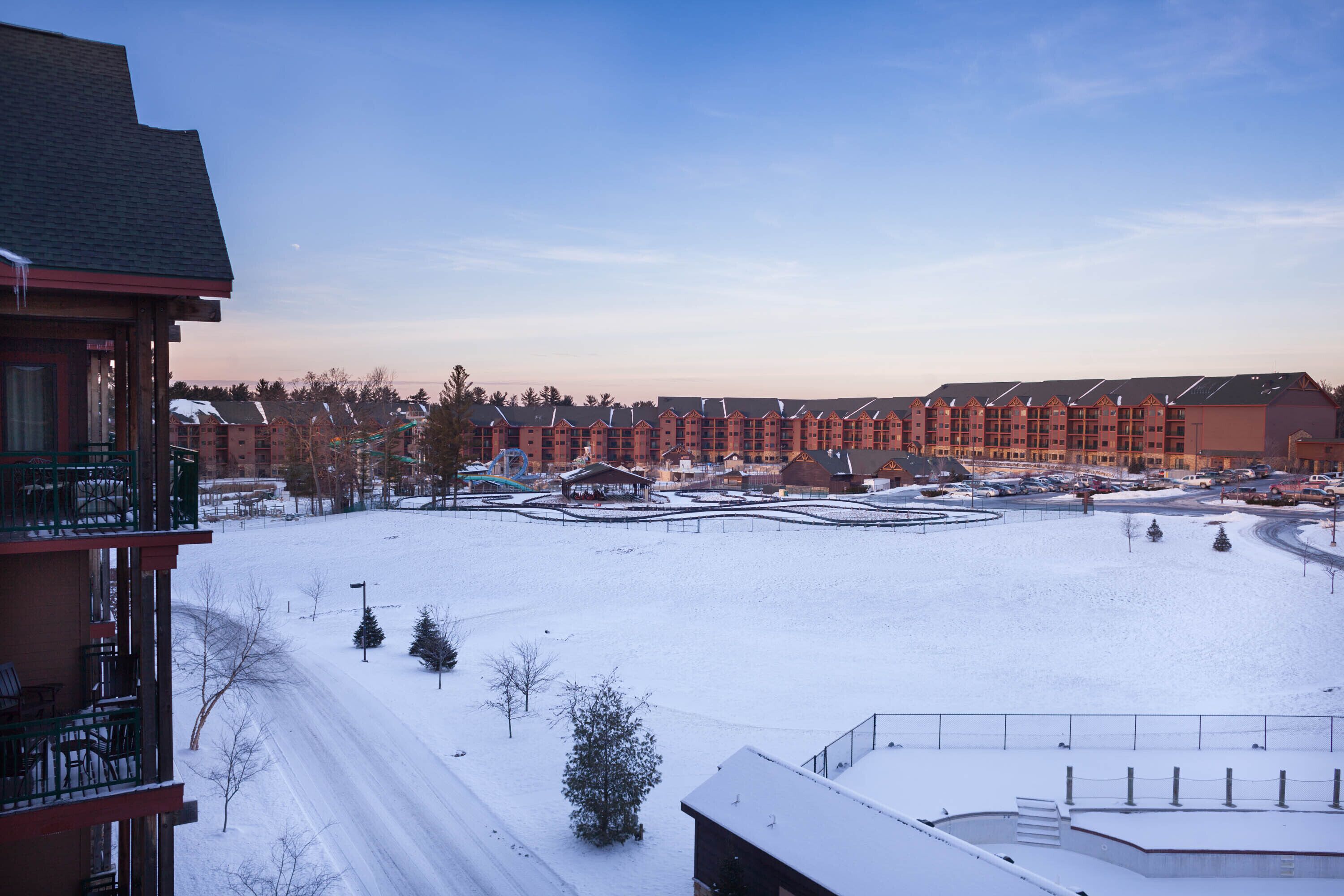 A snow-covered landscape with a row of red buildings, a parking area, and a clear sky.