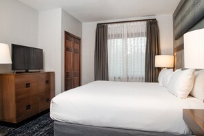 Una habitación de hotel con una cama grande, un televisor sobre un aparador de madera y una ventana con cortinas.