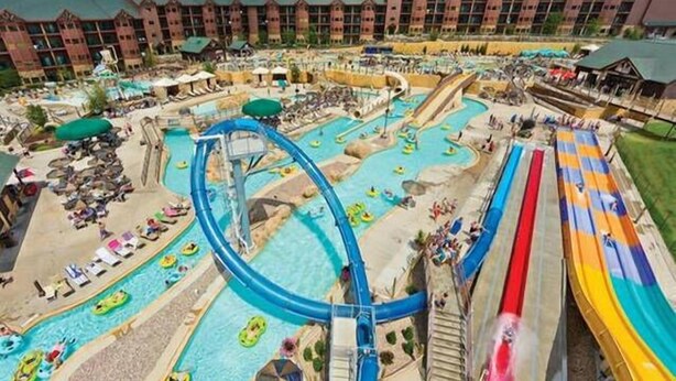 A water park with multiple slides and pools, surrounded by a hotel with a brick facade.