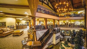 A multi-level hotel lobby with a grand staircase, wooden furnishings, and a Christmas tree.