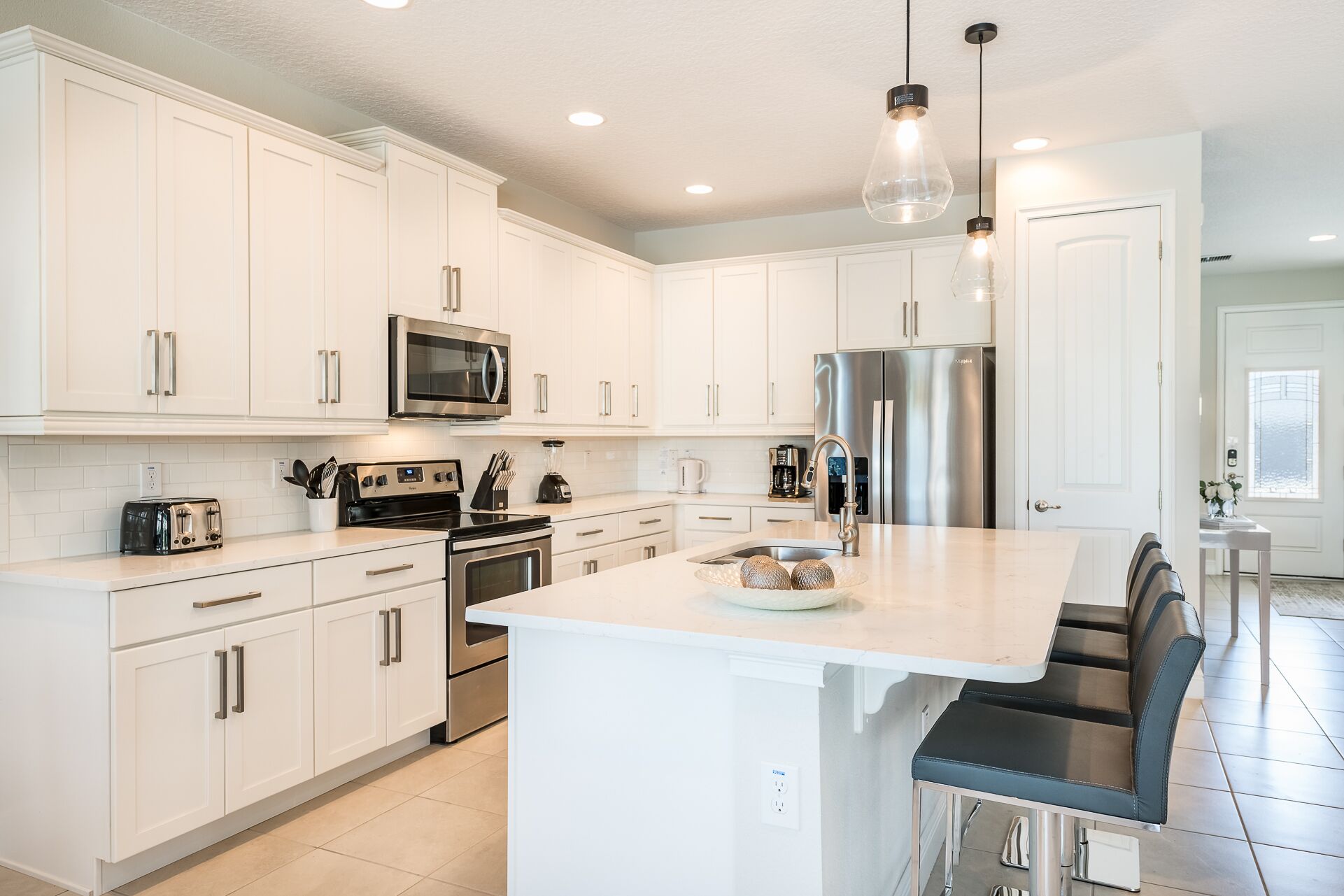 A modern kitchen with white cabinets, stainless steel appliances, a central island with bar seating, and pendant lighting.
