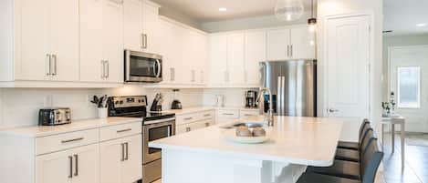 A modern kitchen with white cabinets, stainless steel appliances, a central island with bar seating, and pendant lighting.