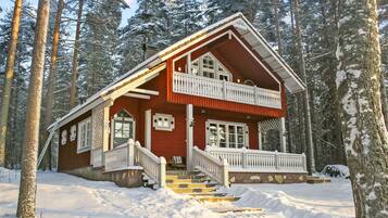 A two-story wooden cabin with a balcony, surrounded by snow-covered trees.