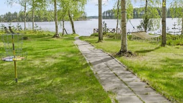 A concrete pathway leading to a lake with a hammock and a disc golf basket.