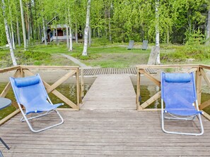 A wooden deck with two blue chairs facing a body of water, surrounded by trees.