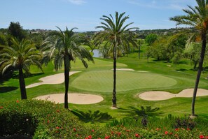 Un campo da golf con bunker di sabbia, palme e una distesa d'acqua sullo sfondo.