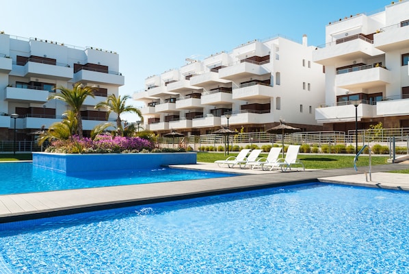 A swimming pool with lounge chairs, surrounded by a landscaped garden and a multi-story building with balconies.