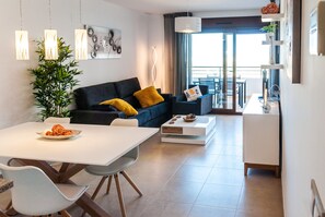 A modern living room with a dining area, a sofa with yellow cushions, a potted plant, and a view to the outside.