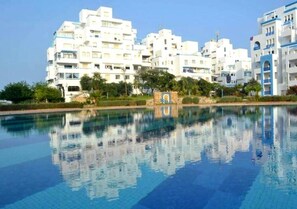 Un hôtel moderne composé de plusieurs bâtiments blancs, doté d’une piscine et entouré de verdure.