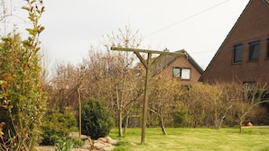 A garden pathway with yellow flowers, a brick wall, and a wooden pergola. - Sun-drenched first floor apartment on the dyke (Puttgarden)
