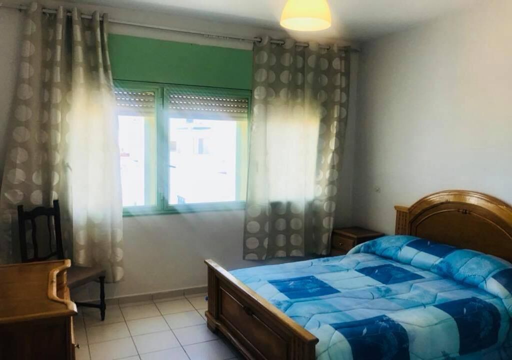 A bedroom with a wooden bed, a chair, a small table, and a window with curtains.