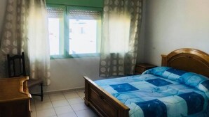 Une chambre à coucher avec un lit en bois, une chaise, une petite table et une fenêtre avec des rideaux.