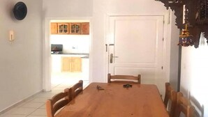 Un coin repas avec une table et des chaises en bois, une porte blanche et une cuisine visible au fond.