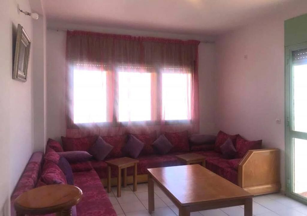 A living room with a large sofa, two small tables, and a window with curtains.