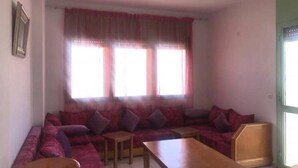 Un salon avec un grand canapé, deux petites tables et une fenêtre avec des rideaux.