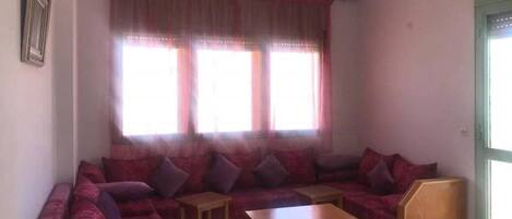 A living room with a large sofa, two small tables, and a window with curtains.