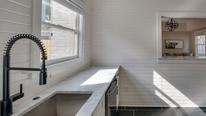 A kitchen with a white countertop, a black faucet, and a window with blinds.