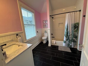 Een badkamer met een marmeren wastafel, toilet, bad en een douchegordijn met bladmotief.