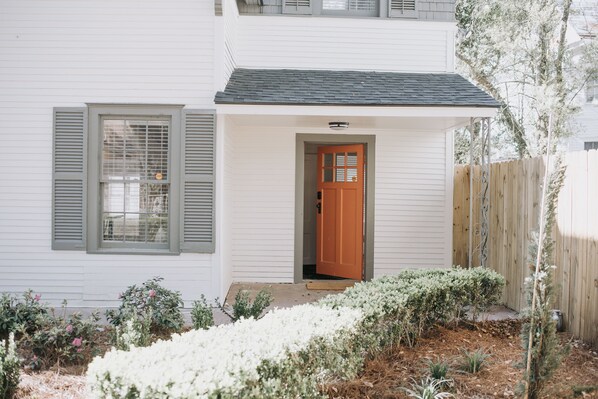 Een wit huis met een houten deur en luiken, een klein terras en een tuin met witte bloemen.