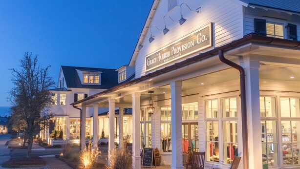 A two-story building with a sign reading "Grace Harbor Provision Co." and a covered front porch with seating. - Broad Creek Cottage in River Dunes (Oriental)