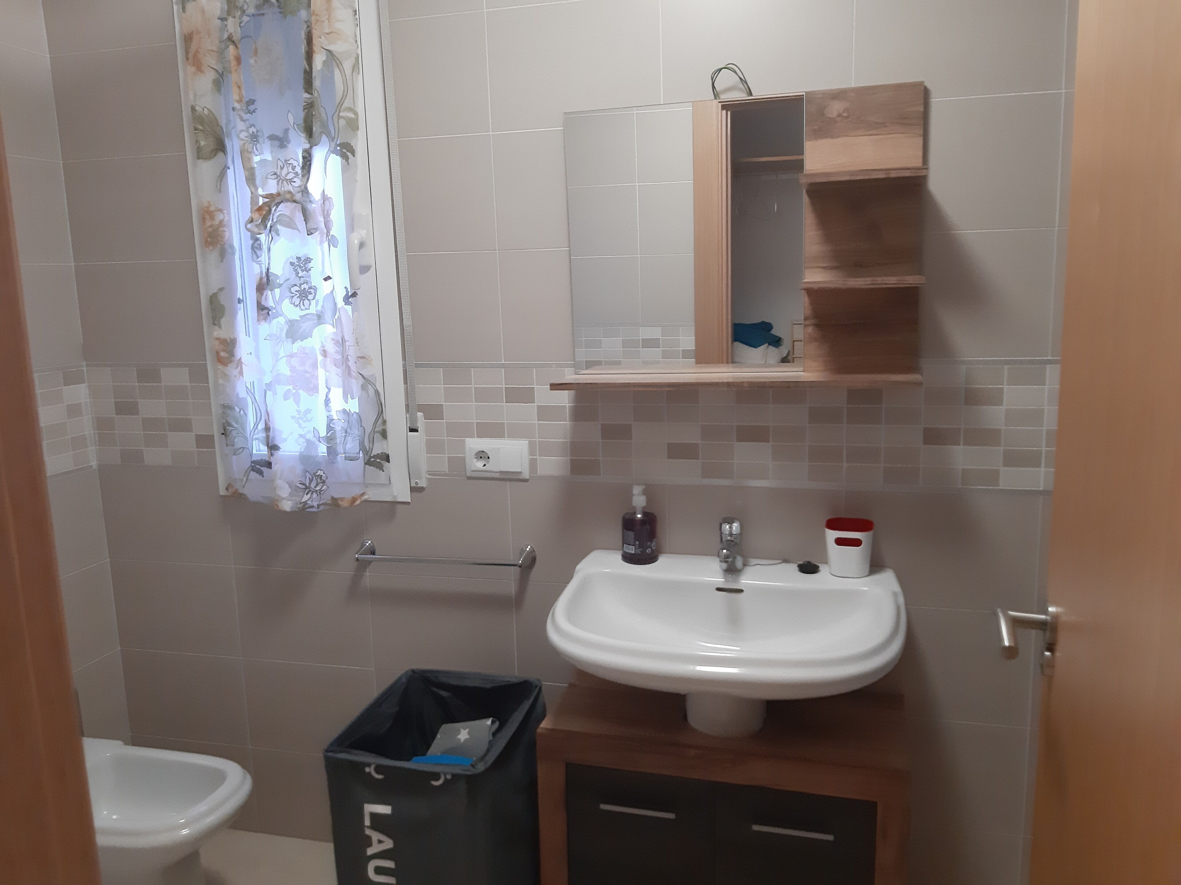 Kylpyhuoneessa on valkoinen pesuallas, peili ja puinen kaappi. Siellä on myös roskakori ja pyyheteline.