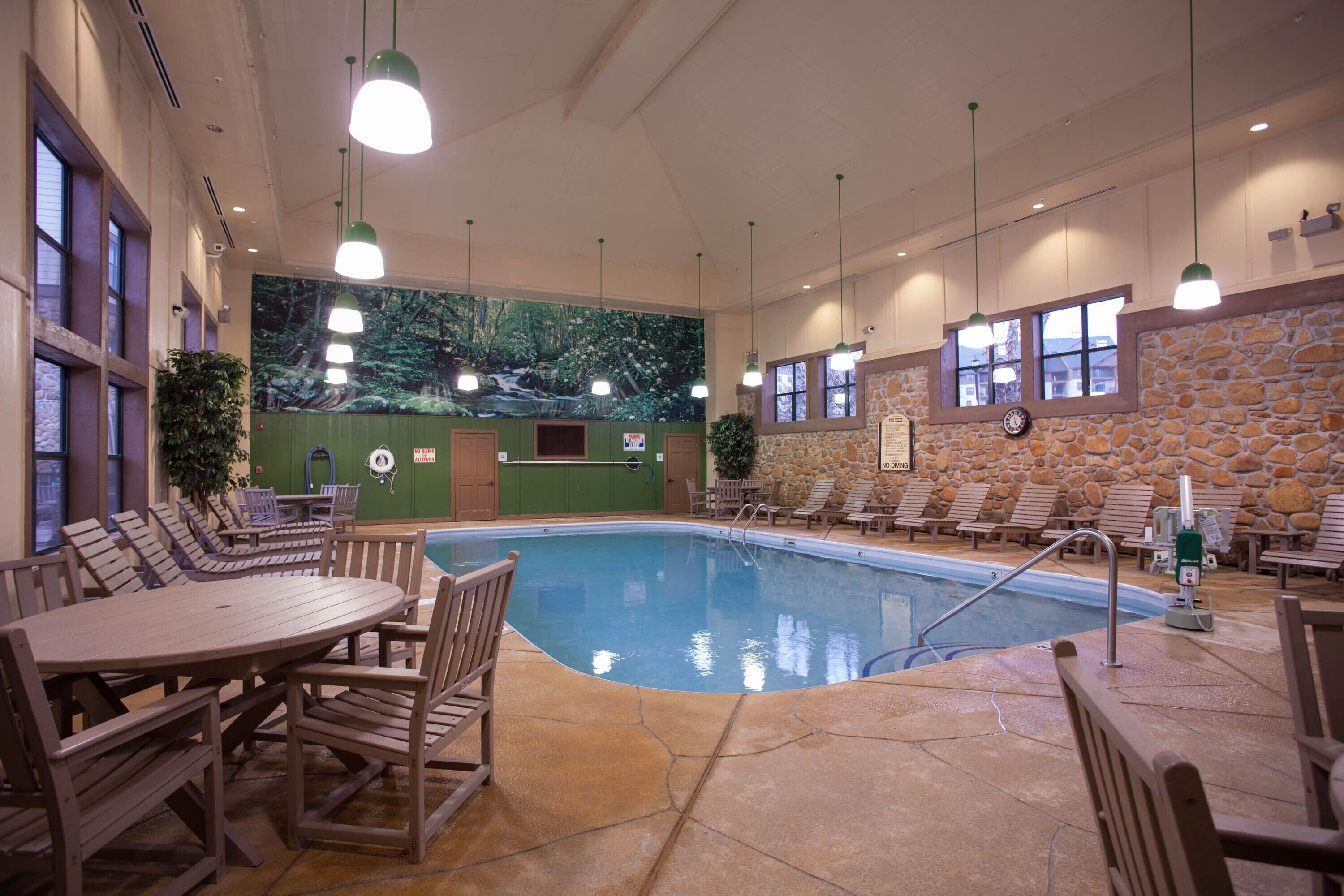 An indoor swimming pool with lounge chairs and a table, surrounded by stone walls and green paneling.