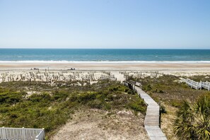 A beach with a wooden boardwalk leading to the shore, sandy dunes, and a clear view of the ocean.