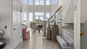 A spacious room with a high ceiling, large windows, a staircase, and a dining area. - Oceanfront with heated private pool (optional),beach access,close to town center (Emerald Isle)