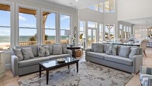 A spacious living room with two grey sofas, a coffee table, and large windows overlooking a beach. - Oceanfront with heated private pool (optional),beach access,close to town center (Emerald Isle)