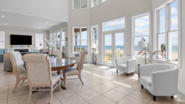 A spacious living room with a large dining table, comfortable seating, and a view of the ocean through large windows. - Oceanfront with heated private pool (optional),beach access,close to town center (Emerald Isle)
