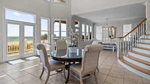 A spacious dining area with a round table and chairs, large windows with ocean views, and a staircase leading to another level. - Oceanfront with heated private pool (optional),beach access,close to town center (Emerald Isle)